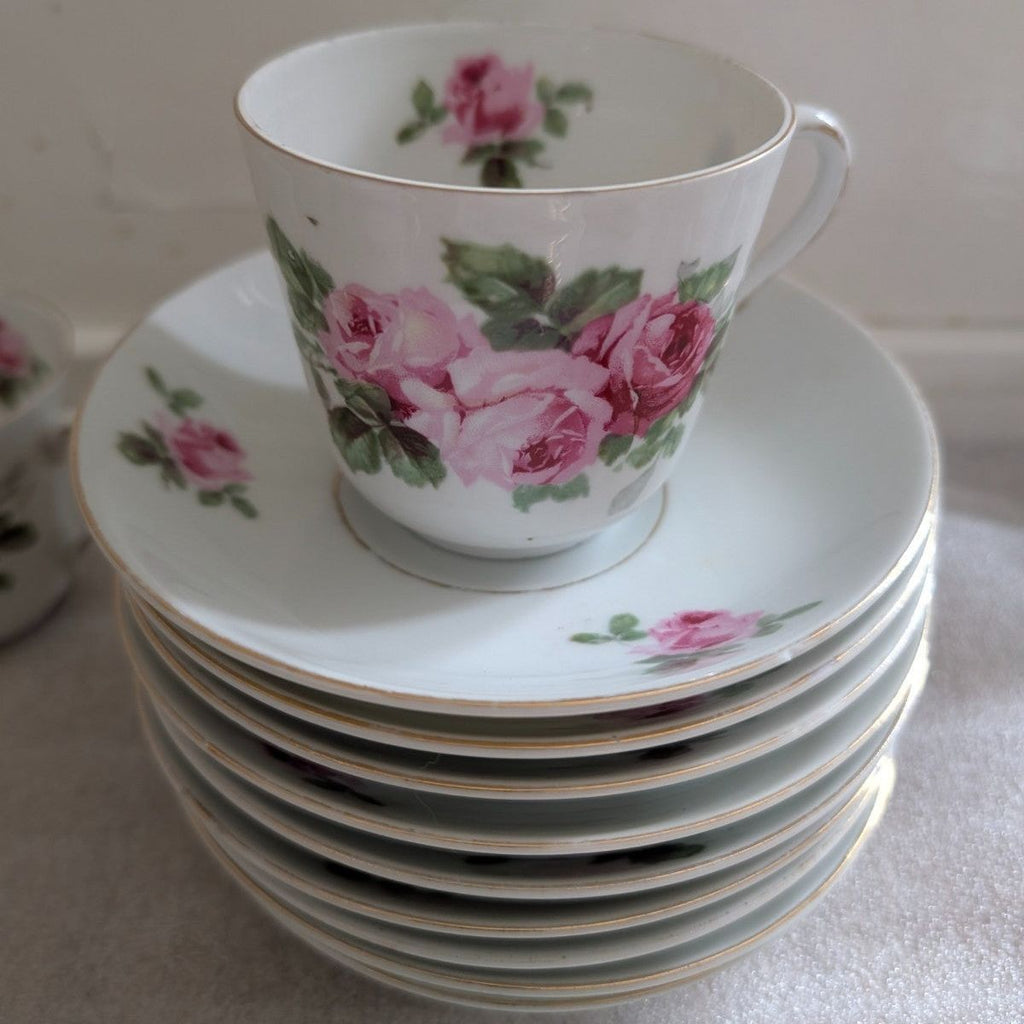 Porcelain teacup and saucer with pink rose floral border, next to stacked plates