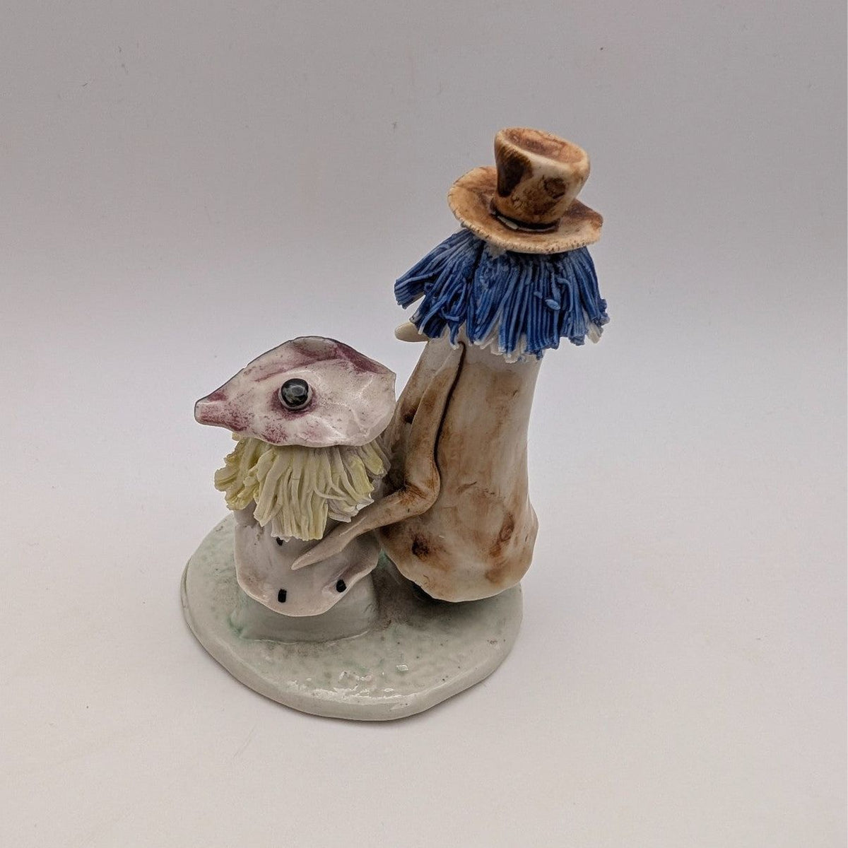 Pottery couple figurine, side view: blue tassel hat figure with seated partner