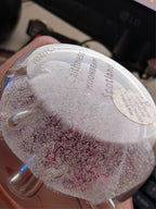 Glass paperweight with pink speckled design and etched circular stamp