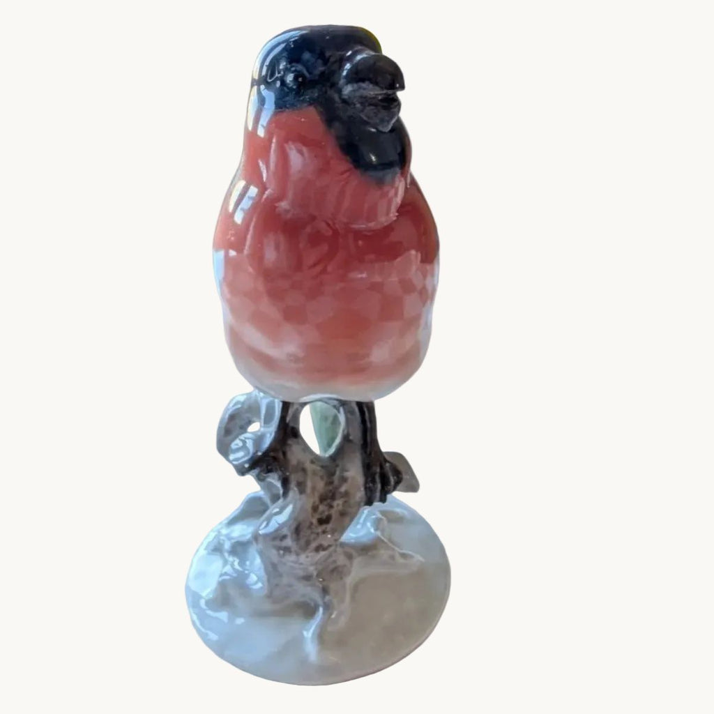 Porcelain bullfinch figurine with pink breast and dark head, standing on base