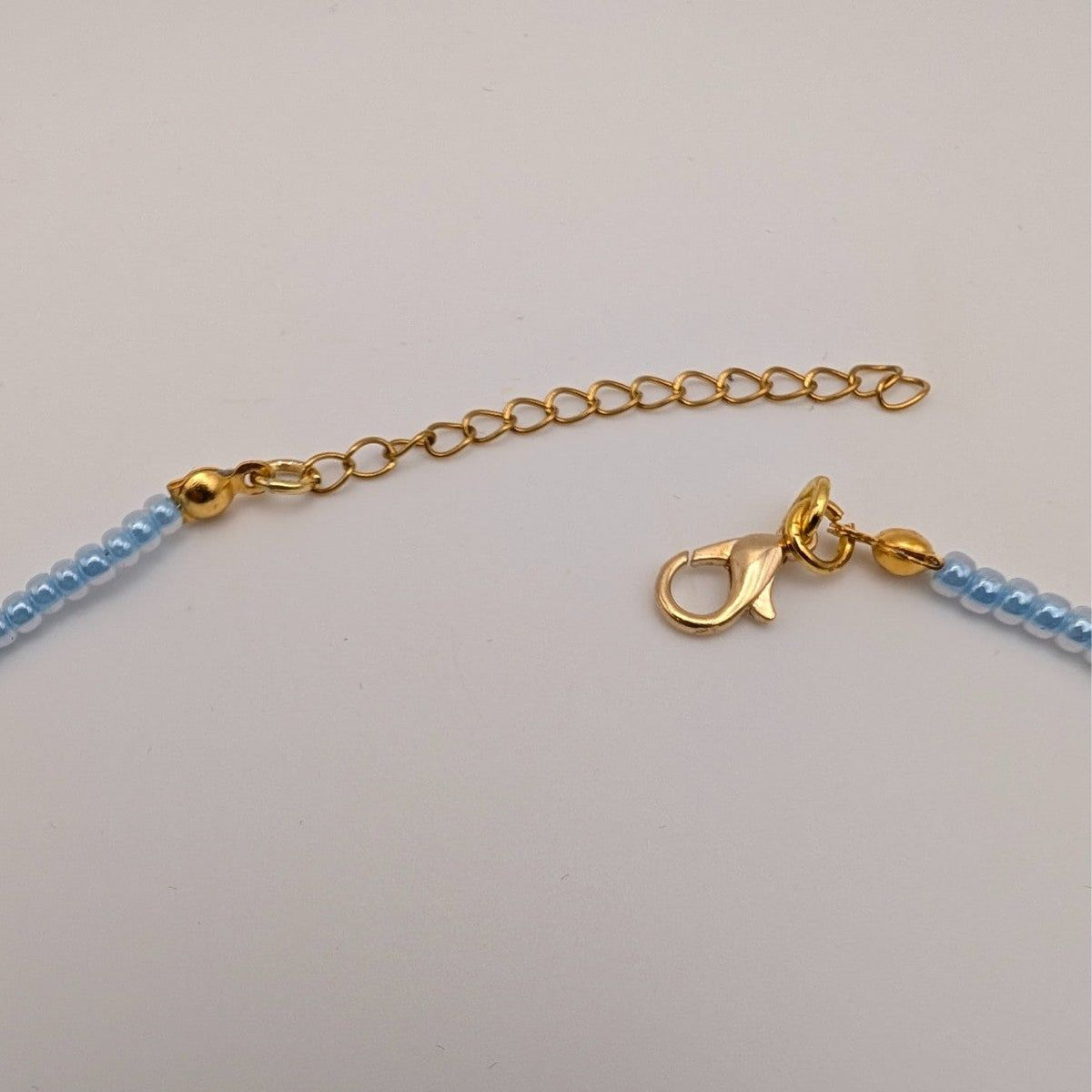 Gold clasp and chain on light blue beaded choker necklace
