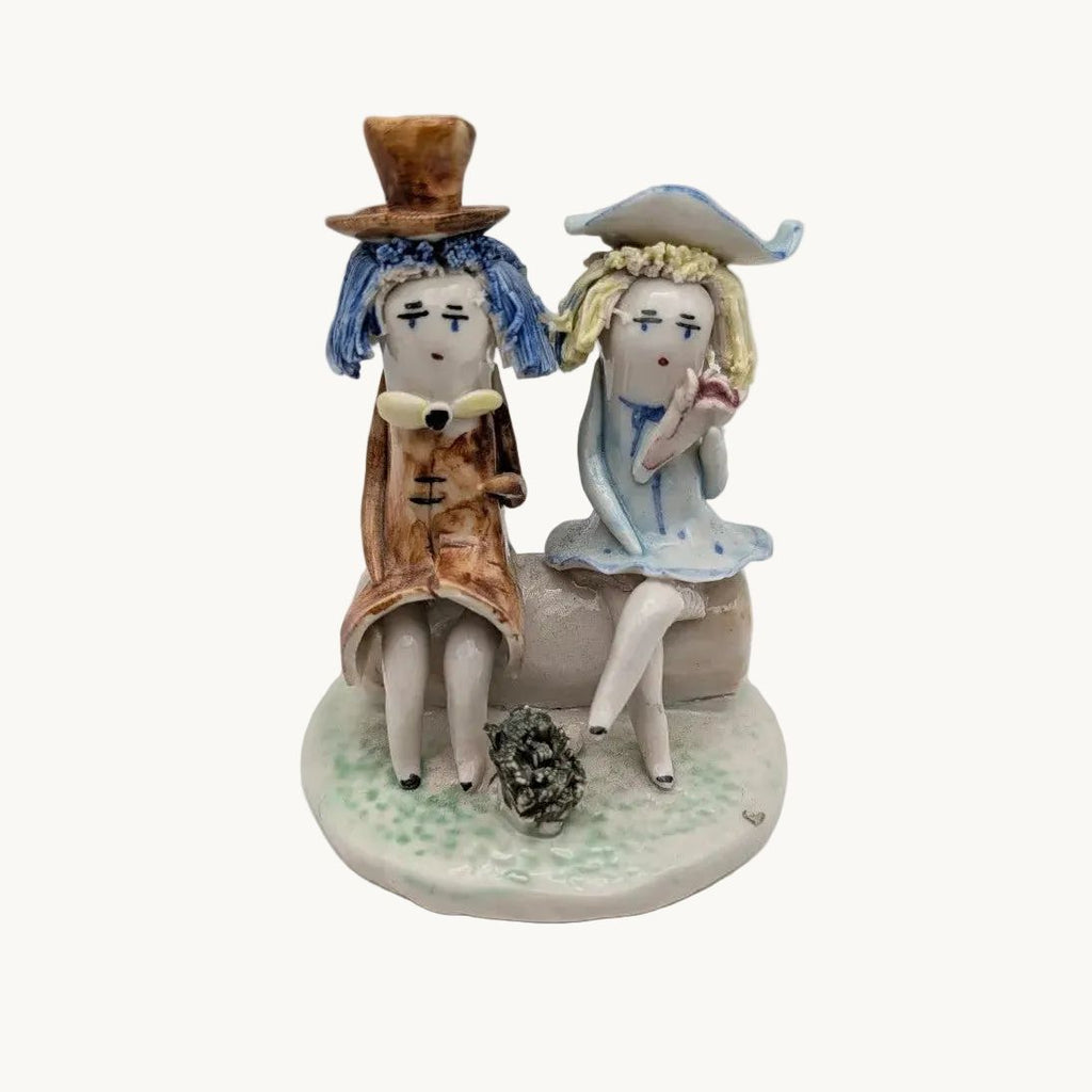 Couple seated on bench pottery figurine, blue-and-white dresses, brown hats, seated pose