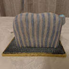 Porcelain figurine back view: seated girl on striped cushioned chaise, on base
