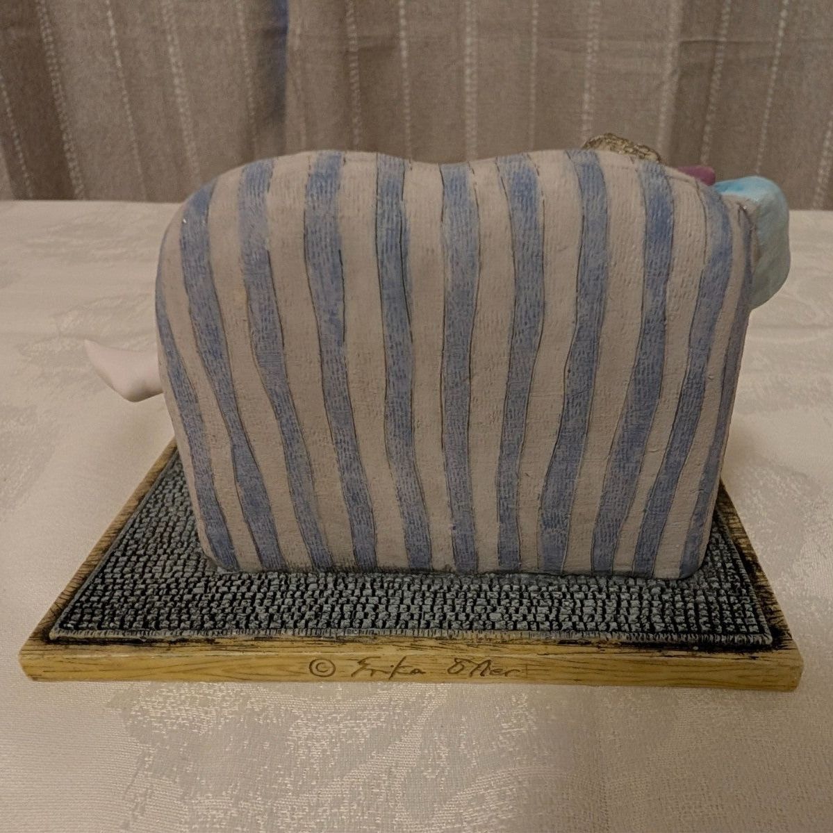 Porcelain figurine back view: seated girl on striped cushioned chaise, on base