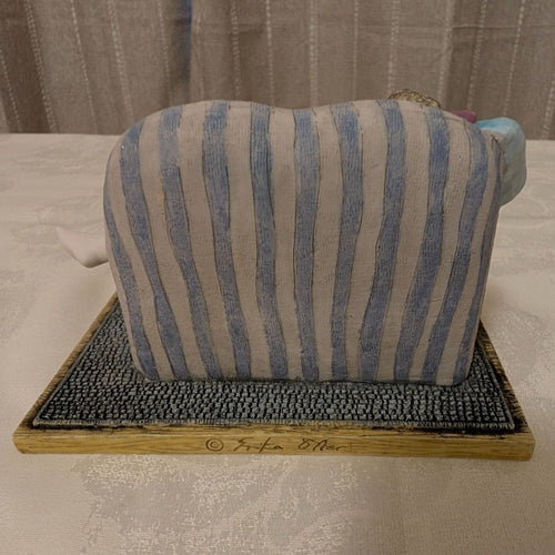 Porcelain figurine back view: seated girl on striped cushioned chaise, on base