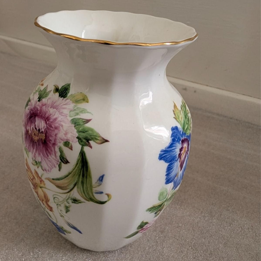 White bone china vase with purple and blue flowers, green leaves, and gold rim