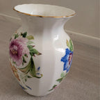 White bone china vase with purple and blue flowers, green leaves, and gold rim