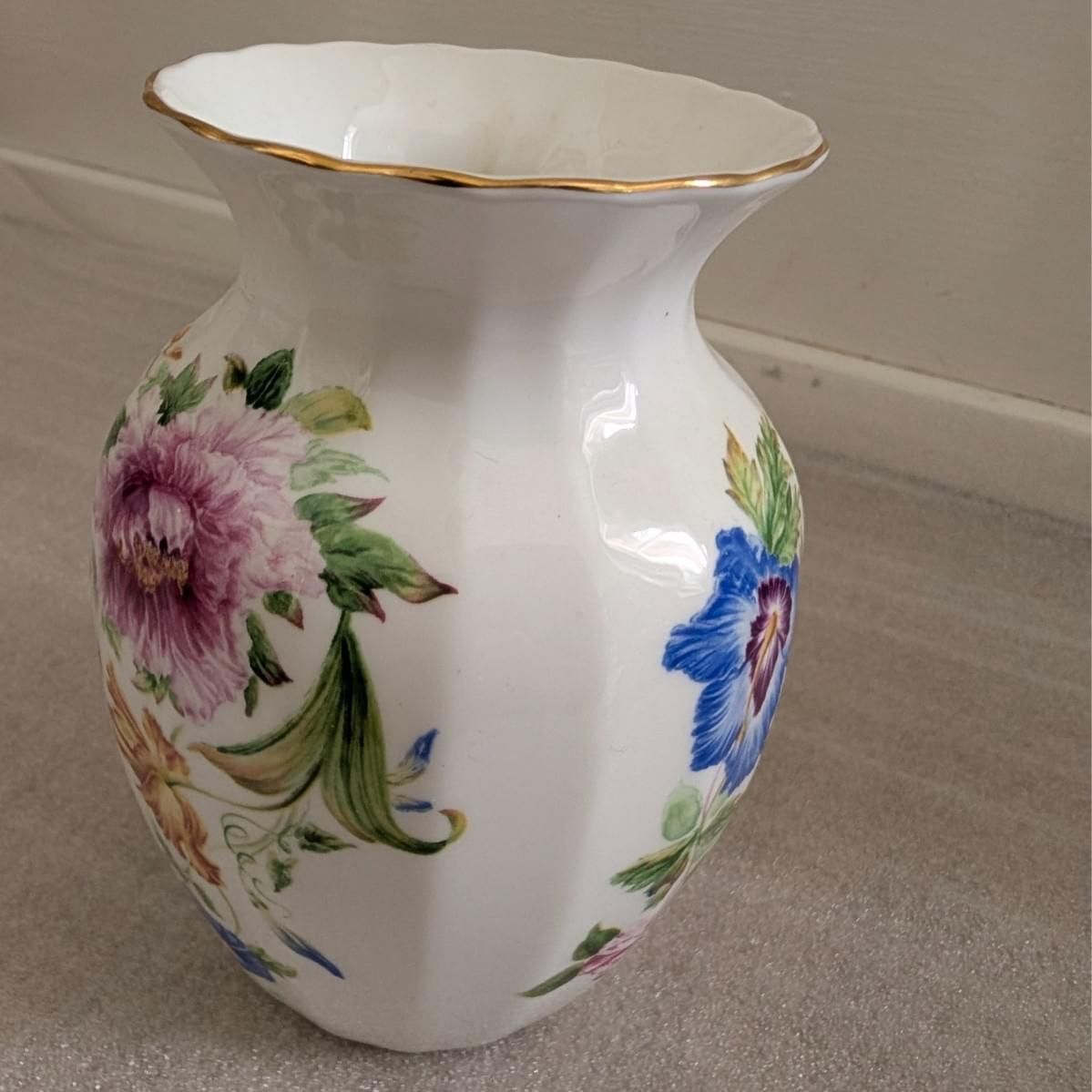 White bone china vase with purple and blue flowers, green leaves, and gold rim