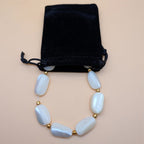 Light blue oval bead necklace on black velvet pouch with gold-tone beads