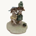Small ceramic figurine of two seated friends on a rounded base, green and blue clothing