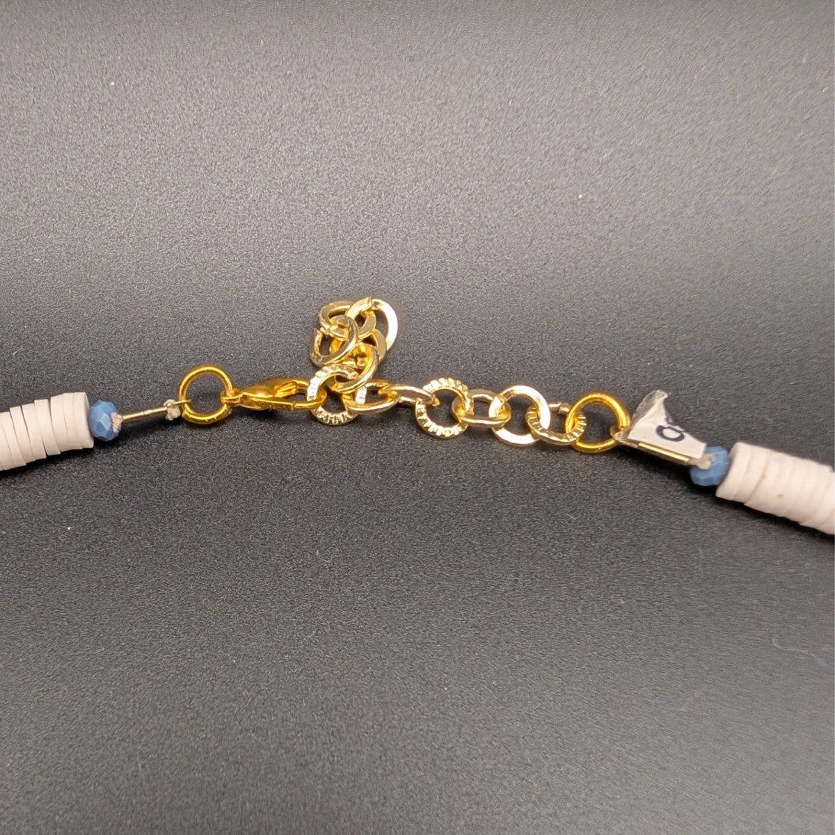 Gold clasp and chain on cream heishi beaded choker with blue accent bead