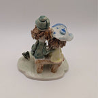 Small ceramic figurine of two friends, one in a cap and green dress, on a rounded base