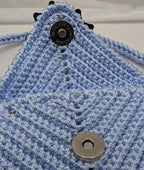 Light blue crocheted phone bag with round tag and snap button on back