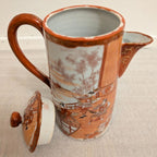 Hand-painted porcelain coffee pot with lid, orange-brown handle, scenic panel