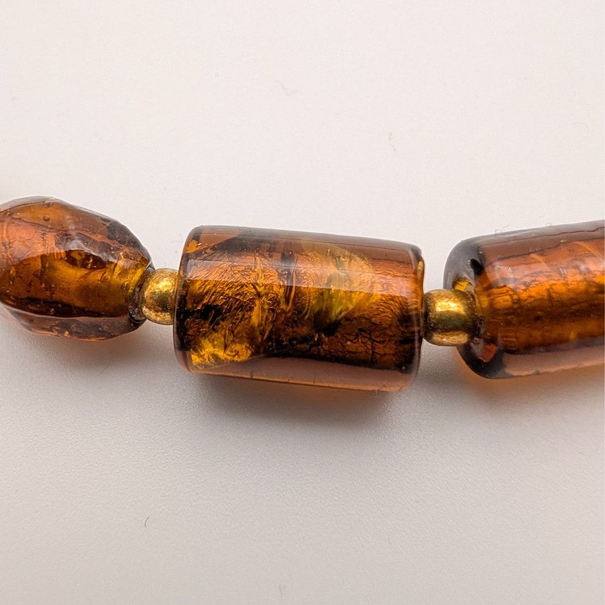 Close-up of amber glass beads: dark amber barrel pieces with gold-tone links