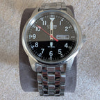 Military style watch close-up, black dial with red second hand and steel bracelet