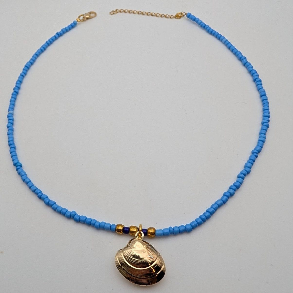 Blue beaded choker necklace with large seashell pendant and small gold bead accents