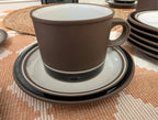 Brown stoneware tea cup with handle on matching saucer and plate