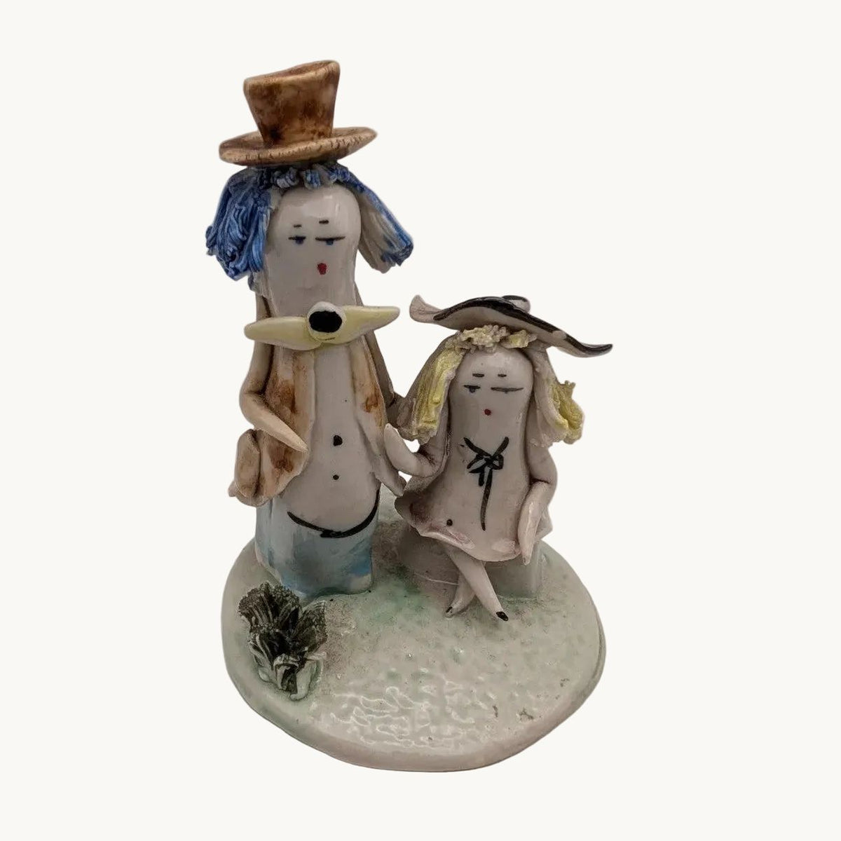 Seated and standing pottery couple figurine with blue-hatted figures and base