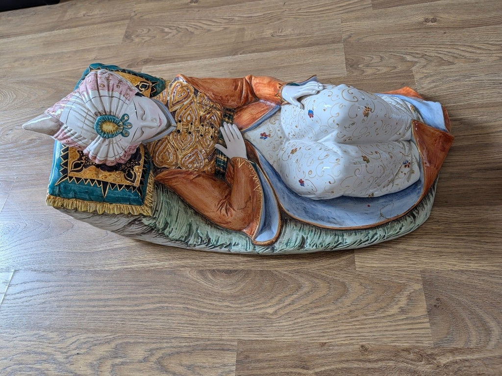 Reclining porcelain sultan figurine with white patterned pants, ornate vest, and turquoise cushion
