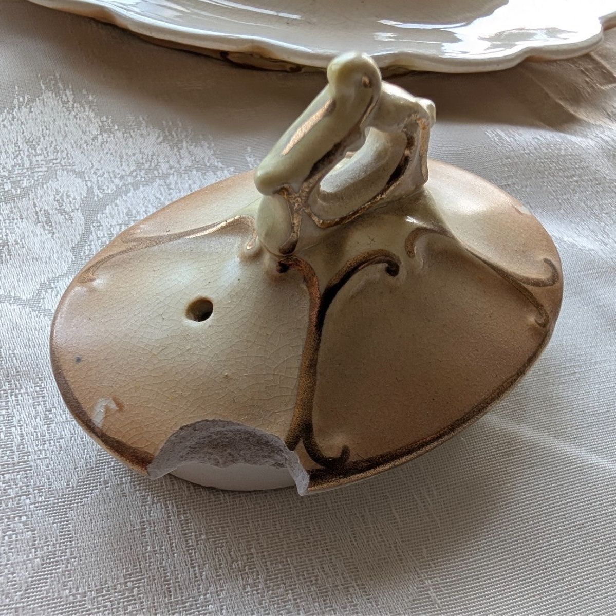 Cream porcelain teapot lid finial detail with gold-toned accents and opening