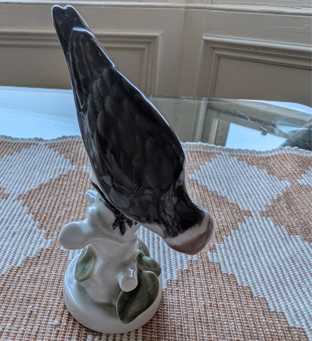 Porcelain woodpecker figurine with dark plumage and white flowers on round base, side view