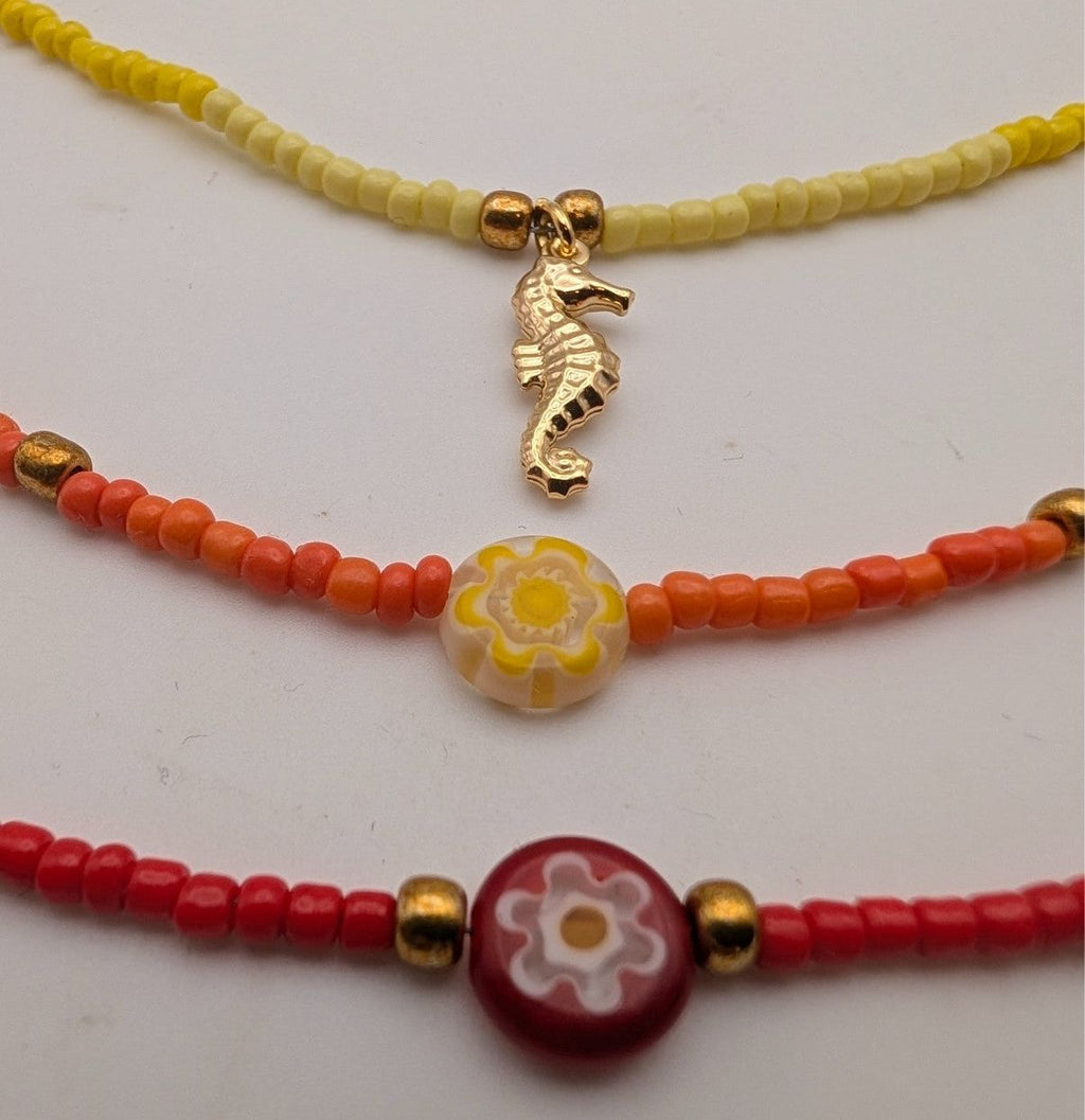 Glass beaded necklace strand with gold seahorse charm and round flower pendant, red/yellow