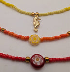 Glass beaded necklace strand with gold seahorse charm and round flower pendant, red/yellow