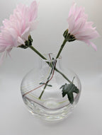 Clear glass bud vase holding two pink flowers with visible internal swirl