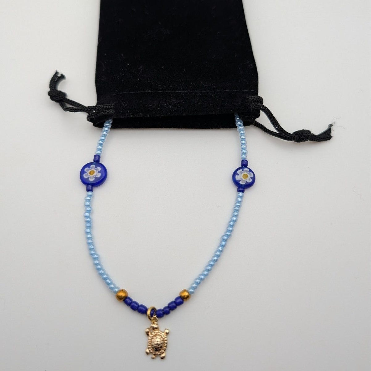 Light blue beaded turtle choker with black cord tie and gold turtle pendant