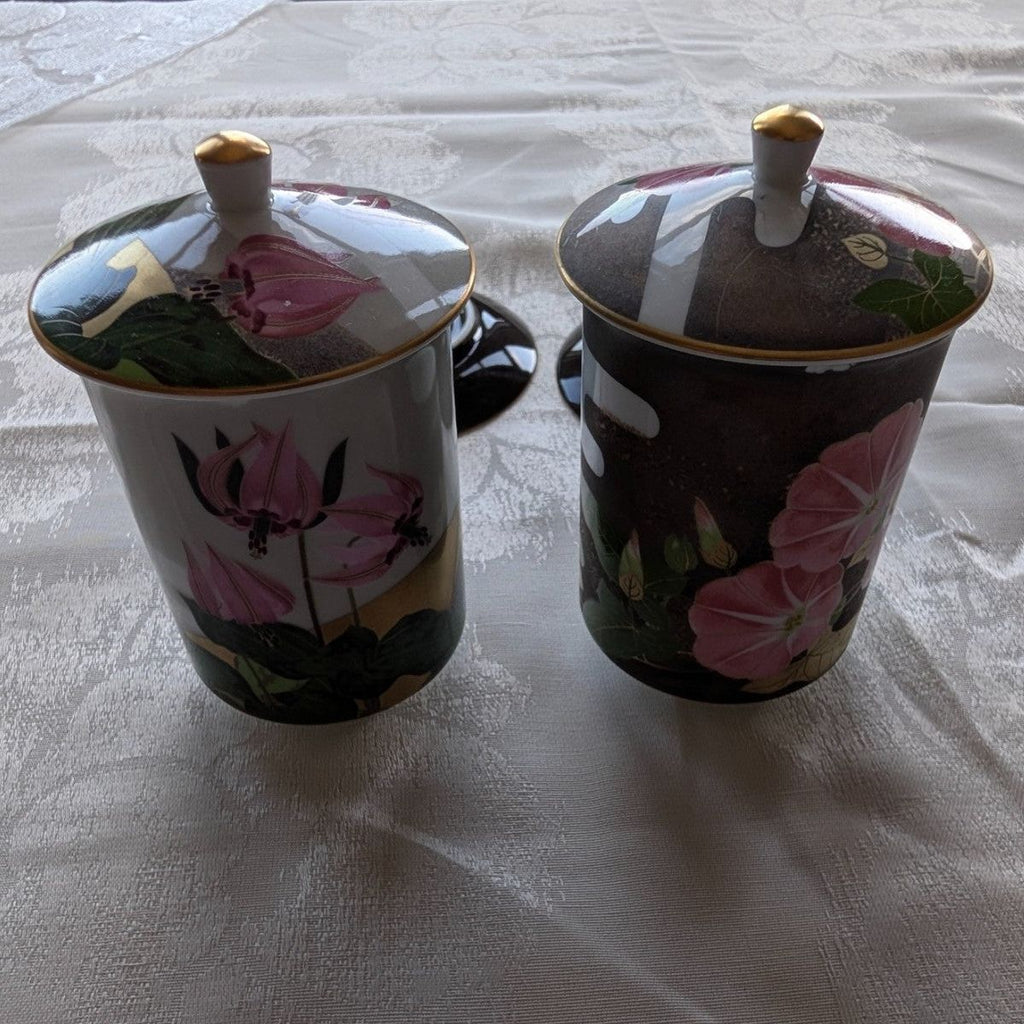 Pair of lidded tea cups, dark ceramic with pink flowers and leafy accents.