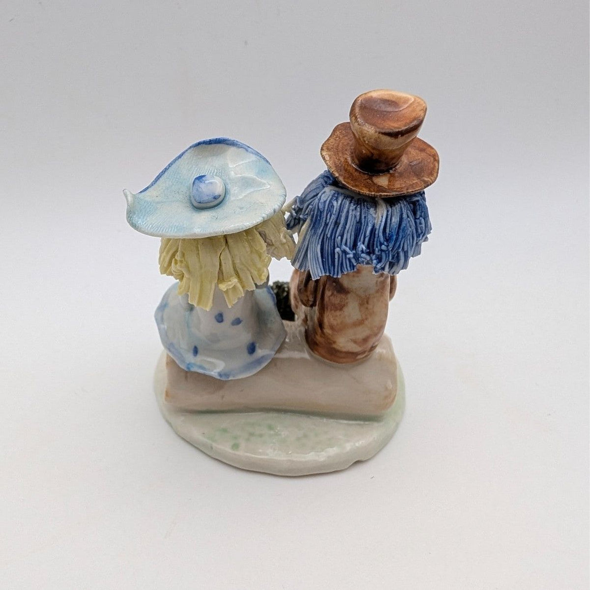 Seated couple on bench pottery figurine, side view, blue outfits and tan hats