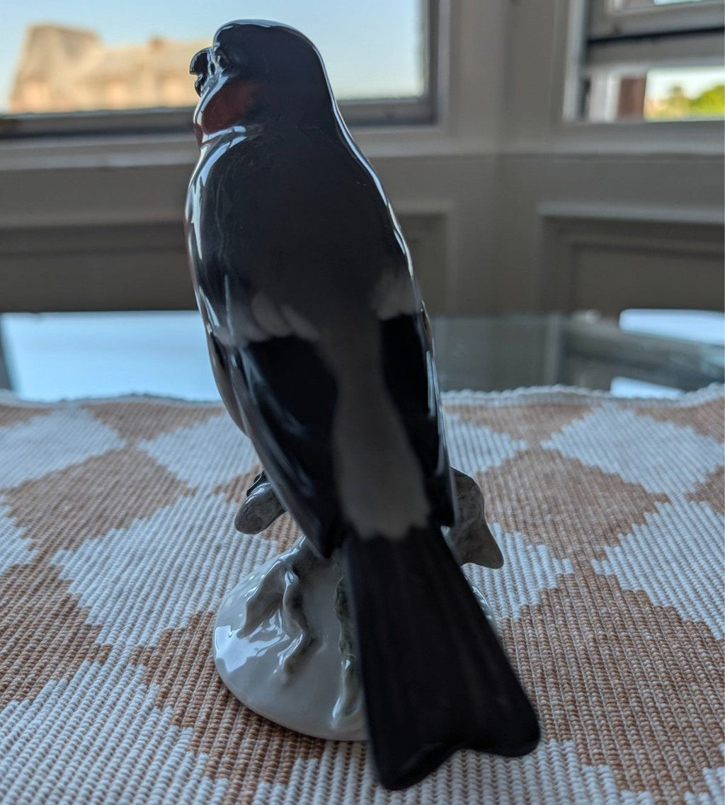 Porcelain bullfinch figurine, glossy dark bird standing on white porcelain base