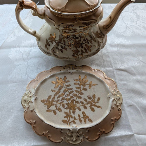 Cream and gold porcelain teapot stand with floral lattice pattern, scalloped rim