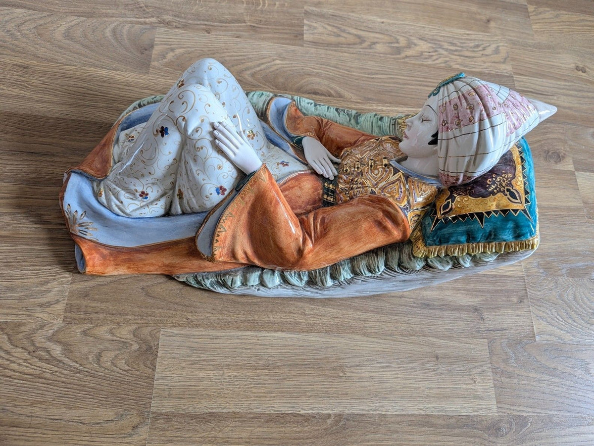 Reclining porcelain figurine on blue cushion with turbaned head, orange vest, and floral robe
