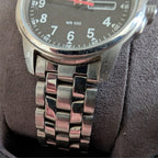 Military style watch close-up, black dial and shiny steel bracelet links