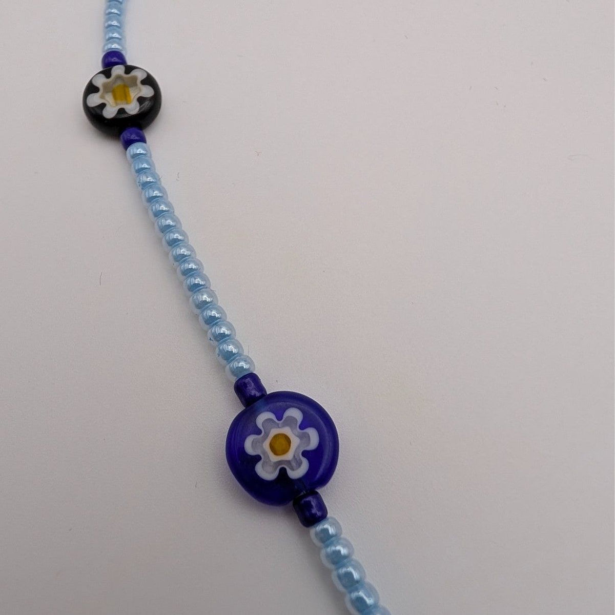 Light blue beaded necklace with blue flower disc charm and dark blue beads