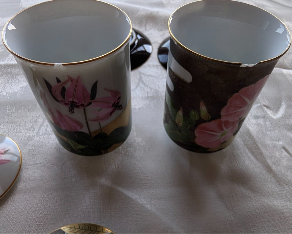 Pair of open tea cups with gold rim, dark ceramic with pink floral design.