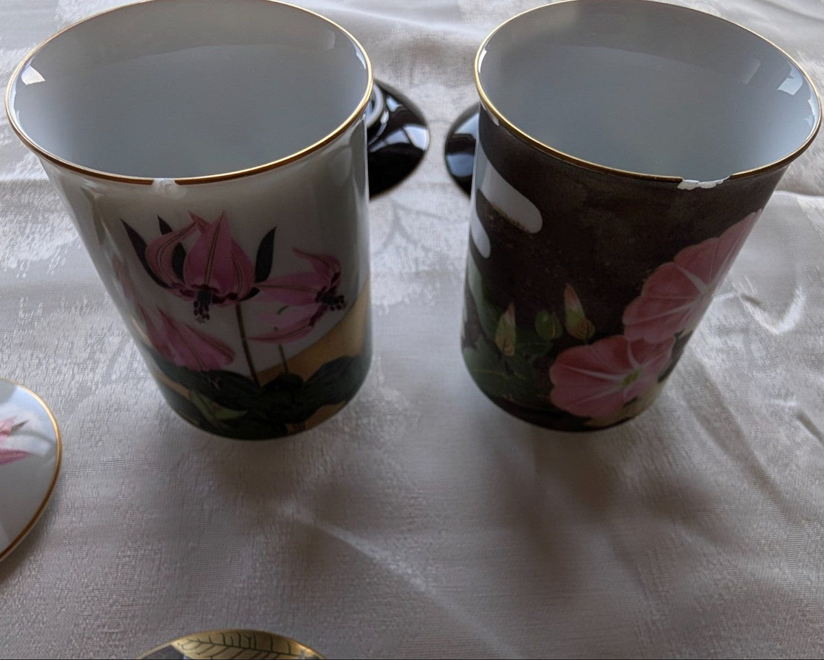 Pair of open tea cups with gold rim, dark ceramic with pink floral design.