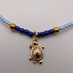 Close-up of light blue bead choker with dark blue accents and gold turtle pendant