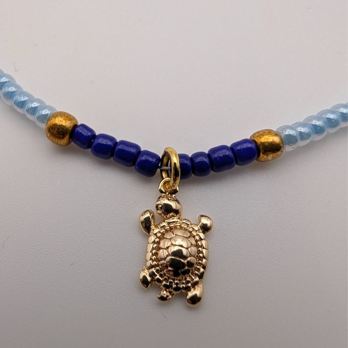 Close-up of light blue bead choker with dark blue accents and gold turtle pendant