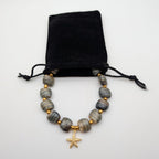 Starfish bead necklace with grey stone beads and gold charm, shown with pouch