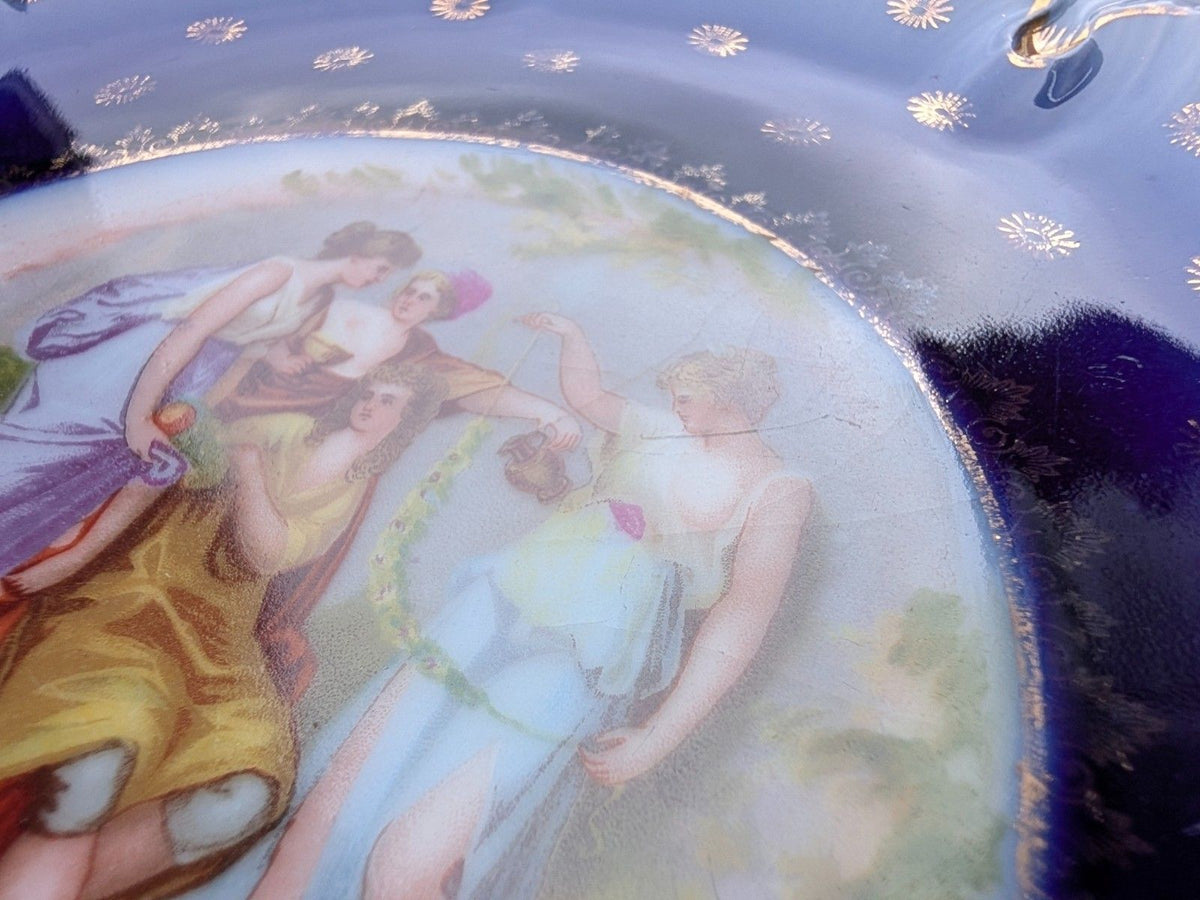 Close-up of painted figures on cobalt blue decorative porcelain plate with gold trim