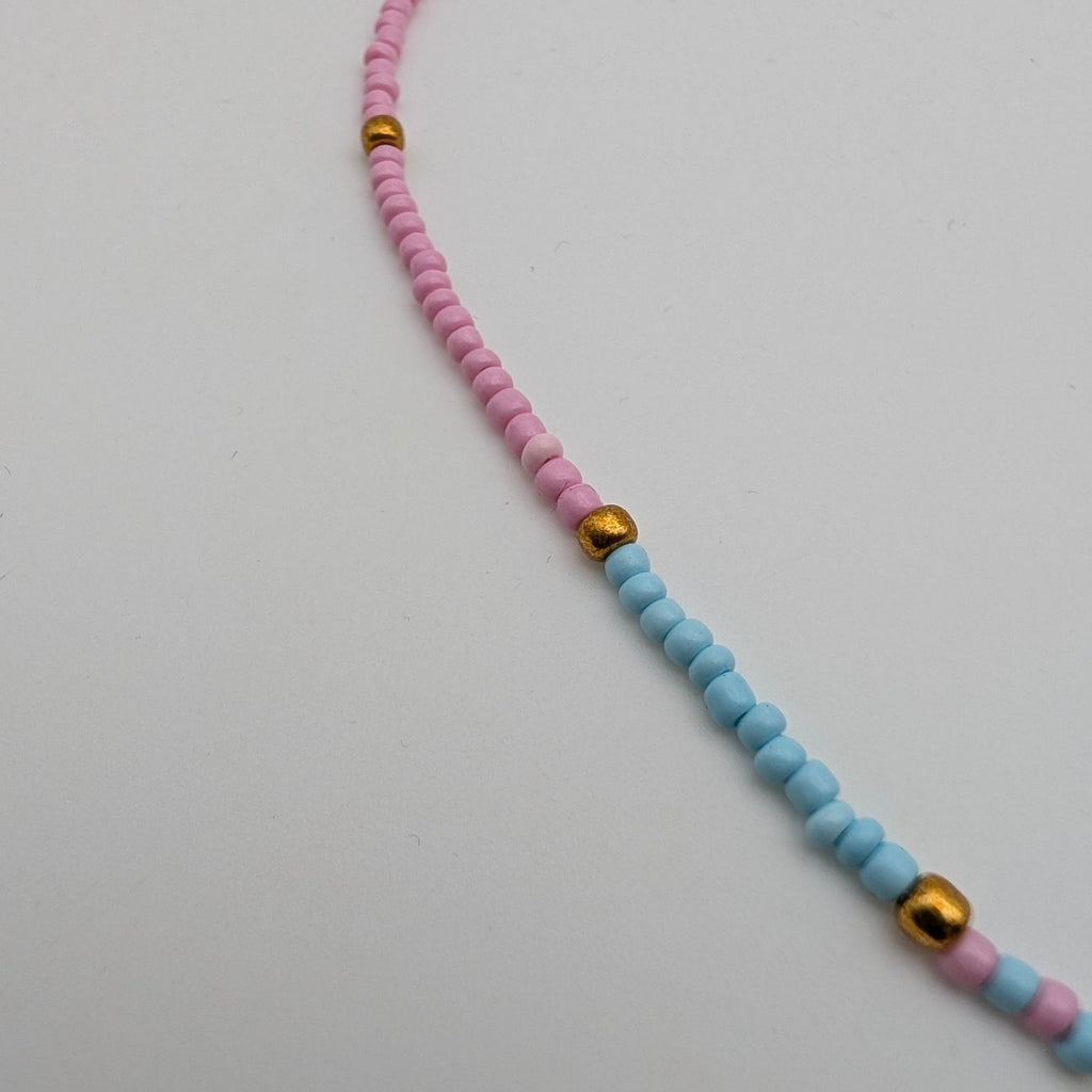 A beaded necklace with alternating strands of pink and light blue beads, accented by small gold spacer beads and a gold-tone clasp, shown on a plain light gray background.