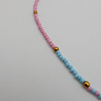 A beaded necklace with alternating strands of pink and light blue beads, accented by small gold spacer beads and a gold-tone clasp, shown on a plain light gray background.
