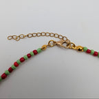 Close-up of a beaded necklace showing red and light green round beads attached to a gold-tone chain extender and lobster clasp, on a plain white background.