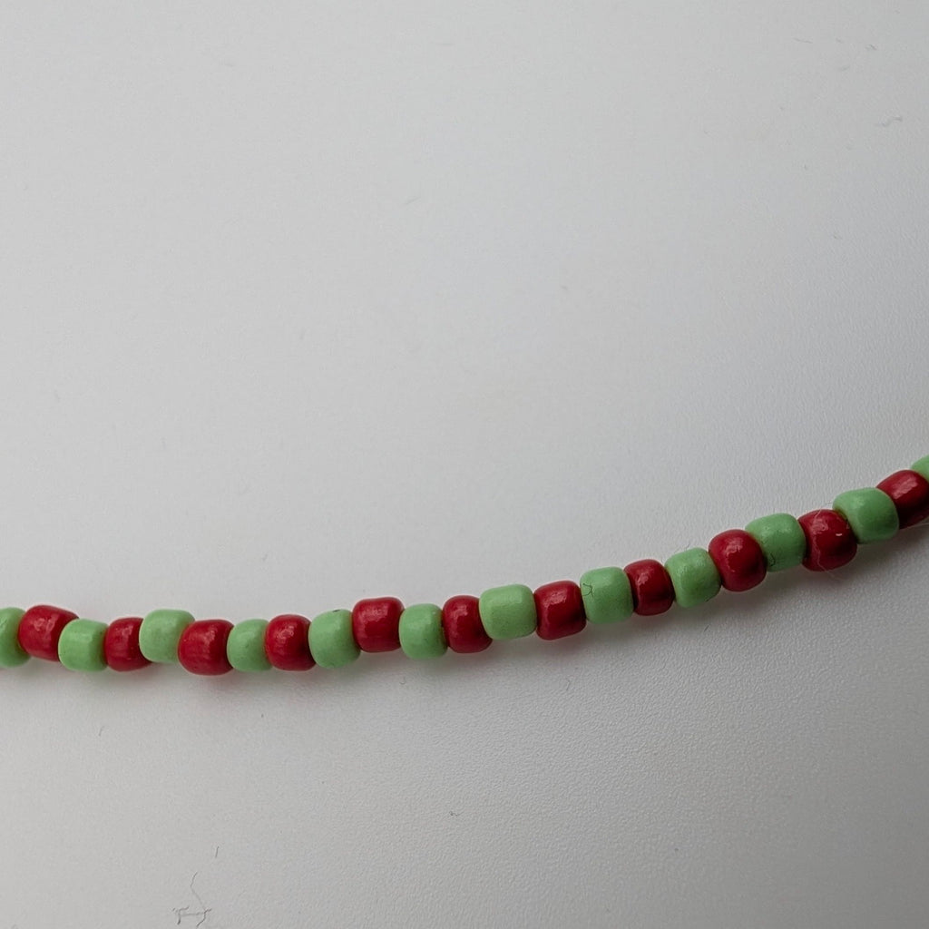 A beaded strand featuring alternating red and light green cylindrical beads, photographed against a plain light gray background.