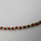 A beaded strand featuring alternating red and light green cylindrical beads, photographed against a plain light gray background.