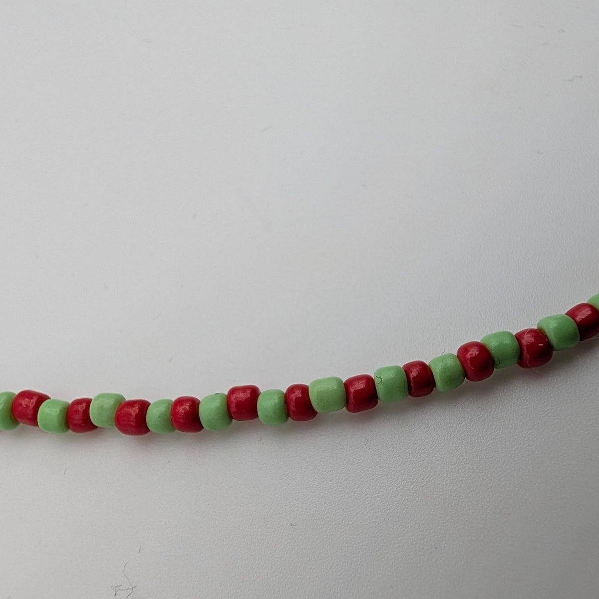 A beaded strand featuring alternating red and light green cylindrical beads, photographed against a plain light gray background.