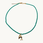 A delicate beaded necklace featuring vibrant turquoise green beads and a small gold-tone dolphin pendant.